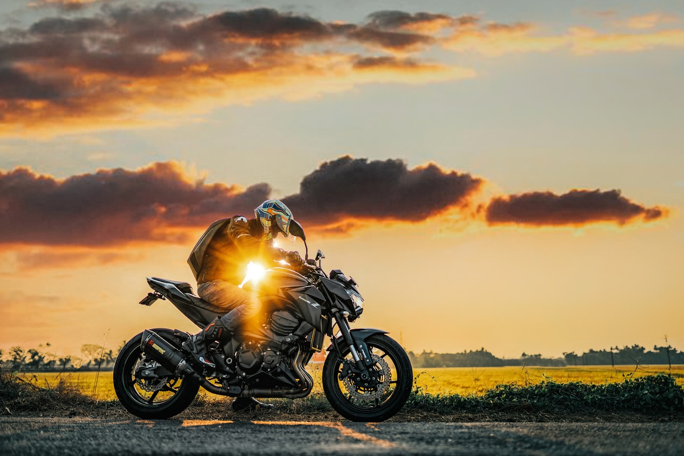 Rider leaning over a naked sport motorcycle as the sun sets behind an open field