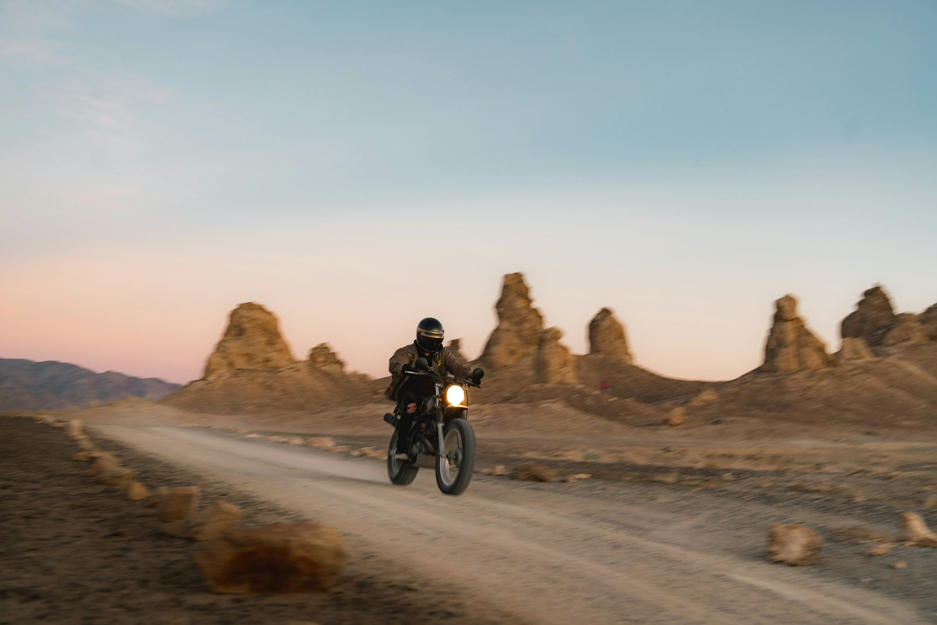 Motorcyclist riding a desert road at dusk, rock spires on the horizon